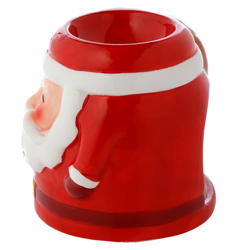 Smiling Santa Claus ceramic oil burner with glowing tealight inside, wax melting in dish, surrounded by Christmas lights and pine branches