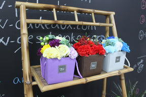 Three soap flower boxes on a bamboo stand against a chalkboard background