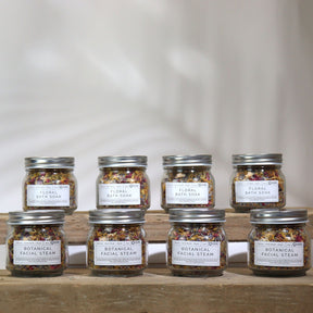 Set of eight jars labeled 'Floral Bath Soak' on a wooden surface with a neutral background