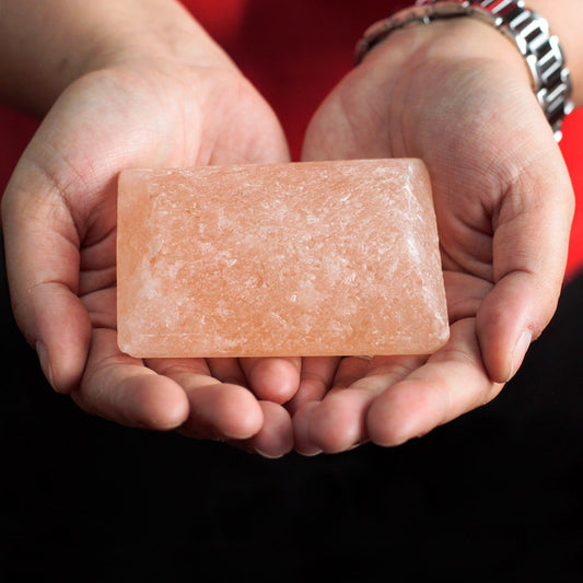 Person holding a pink Himalayan salt bar deodorant against a red background