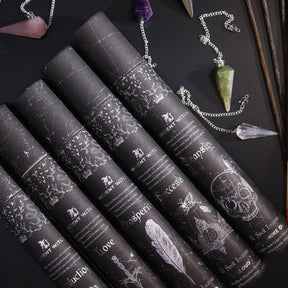 Set of black incense containers with decorative labels on a dark surface with pendulum.