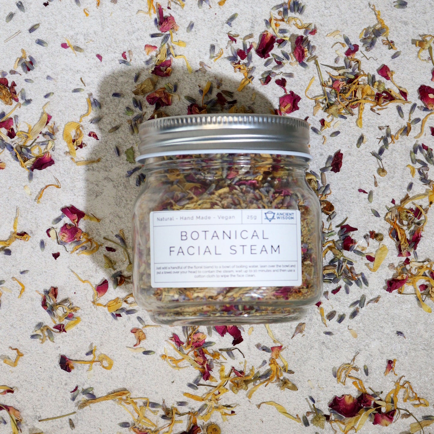 250g jar of dried lavender buds, rose petals, chamomile & calendula flowers spilling onto white marble with steaming bowl in soft spa setting