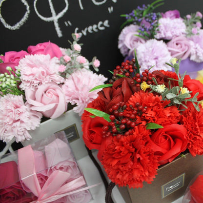 Soap flowers including red, pink, and blue, in a store setting with a blackboard in the background.
