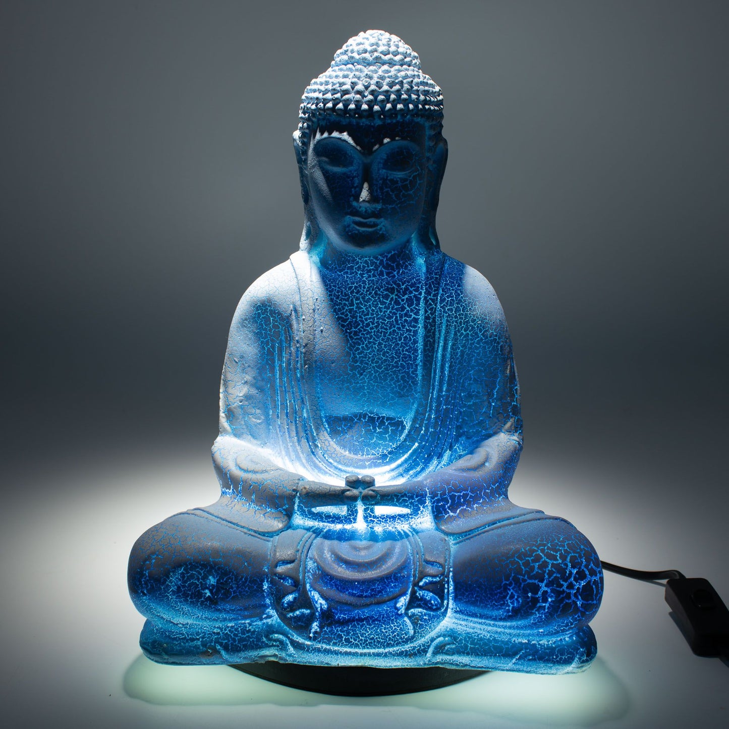 Meditation Buddha Lamp with crackle textured surface on modern oval stand, emitting soft warm ambient glow in a calm living space with subtle lighting