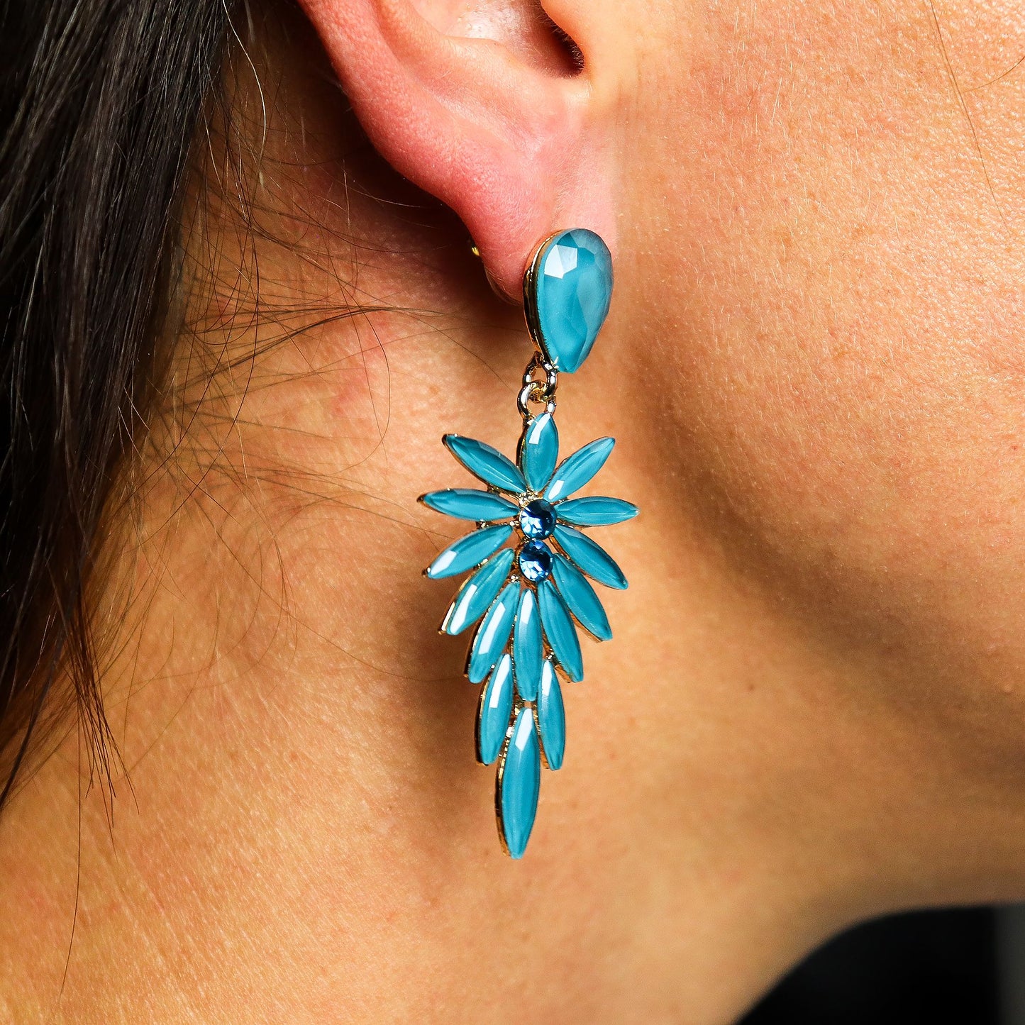 Close-up of a turquoise floral earring worn on an ear.