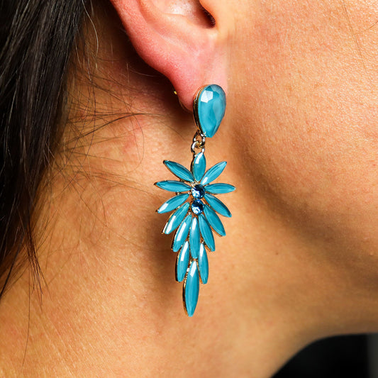 Close-up of a turquoise floral earring worn on an ear.