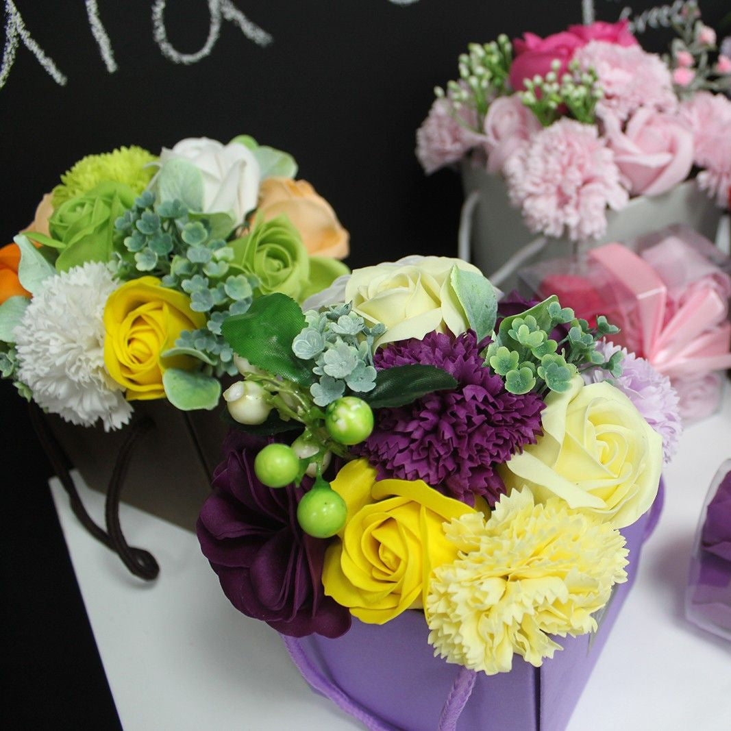 Colorful soap flower arrangements in boxes on a table with a blackboard background
