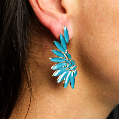 Teal green angel wing earrings with translucent vintage glass and silver stainless steel, hanging against forest backdrop with soft sunlight