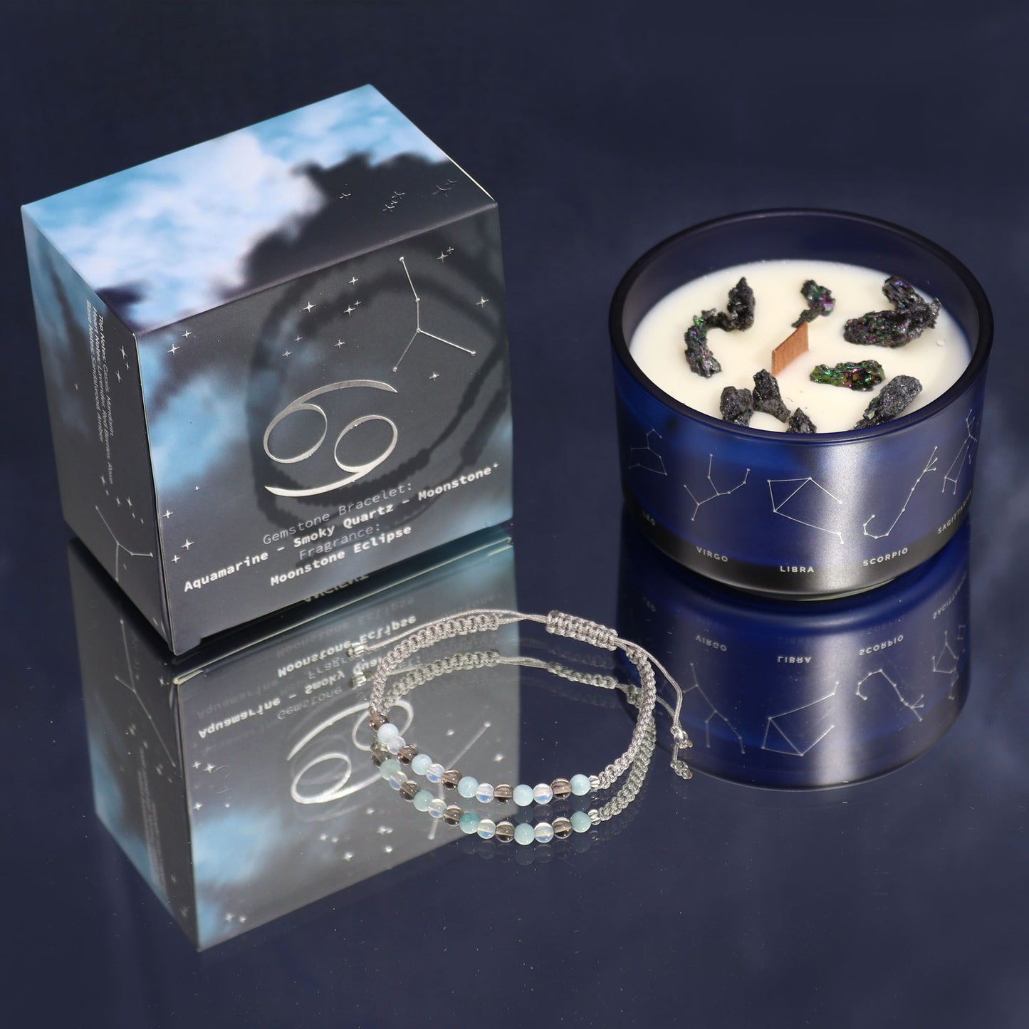 Blue candle with star design, packaging, and bracelet on a reflective surface