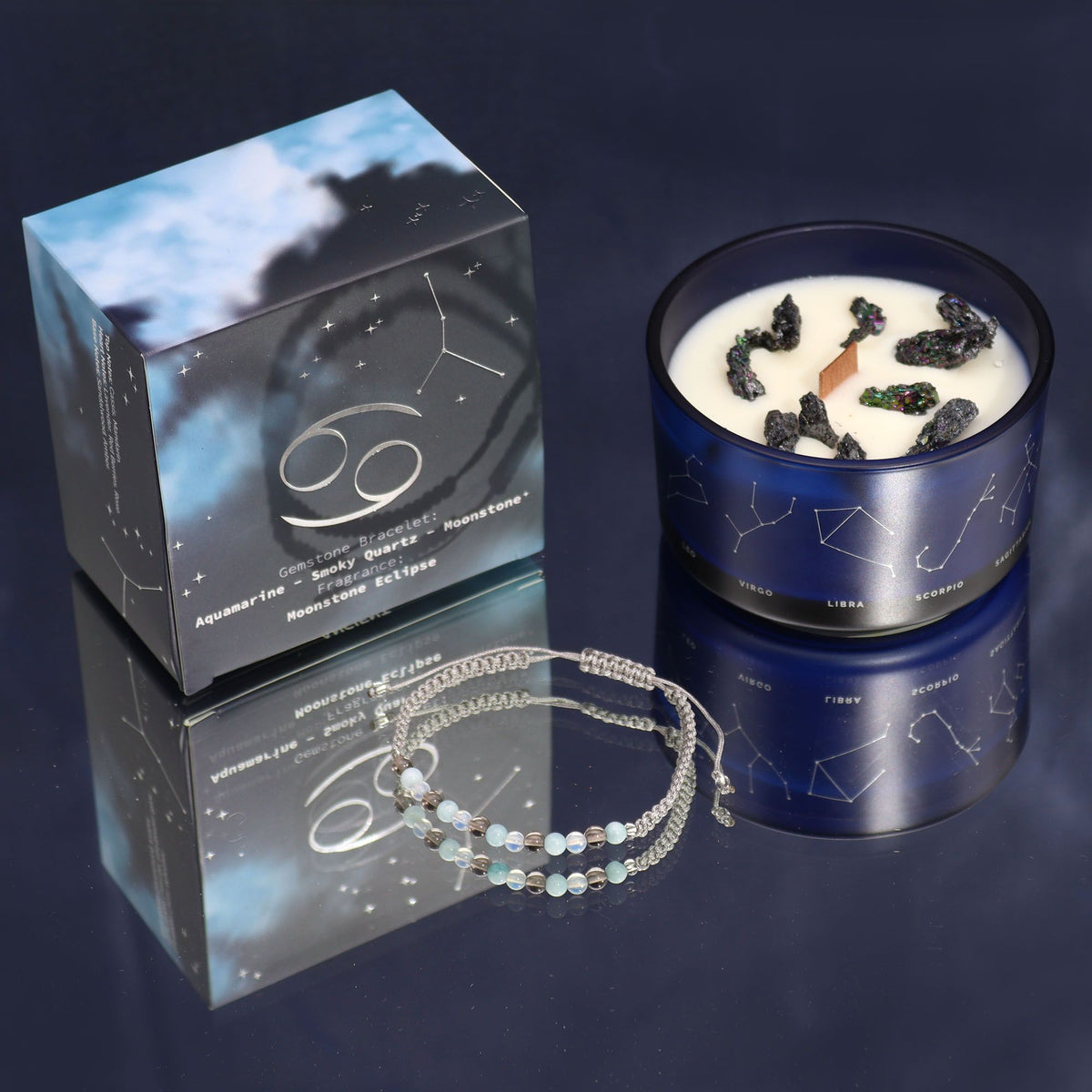 Blue candle with star design, packaging, and bracelet on a reflective surface