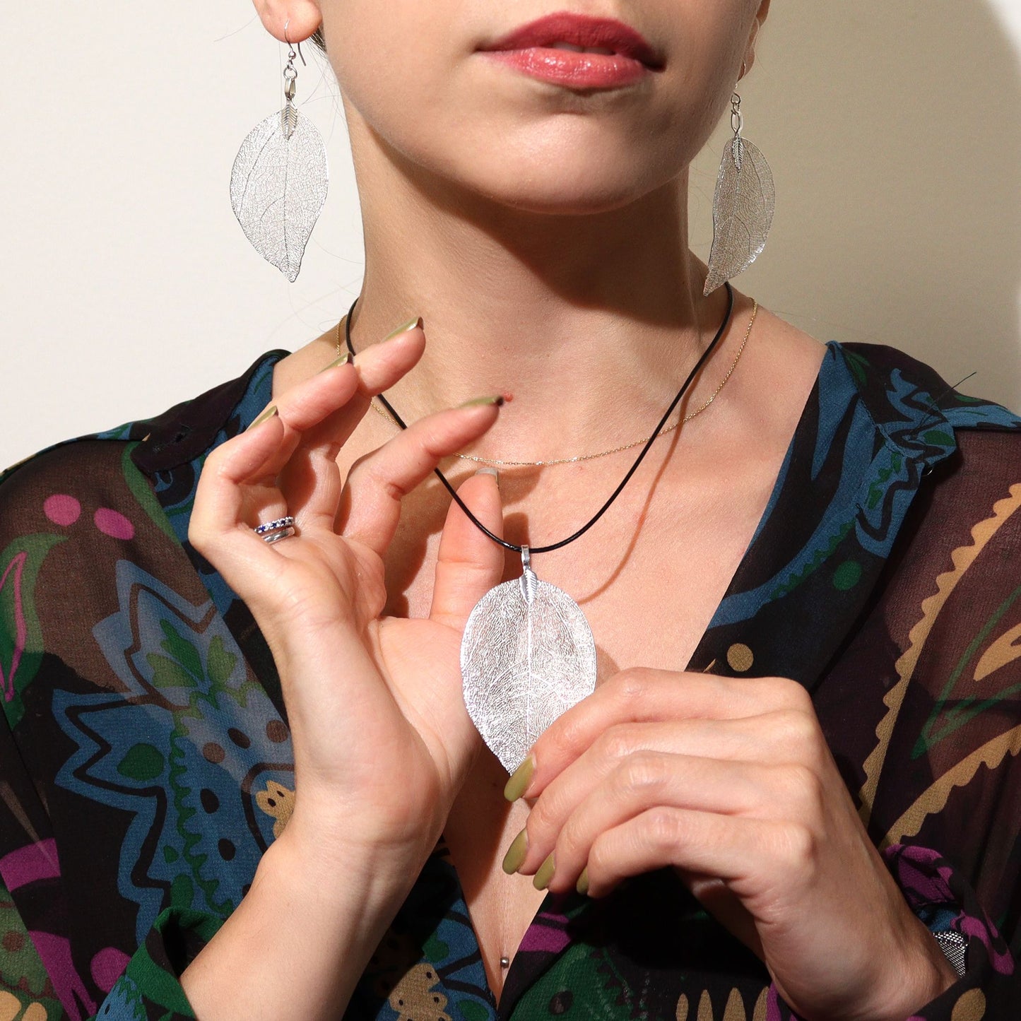 Person wearing a silver leaf-shaped pendant necklace and earrings