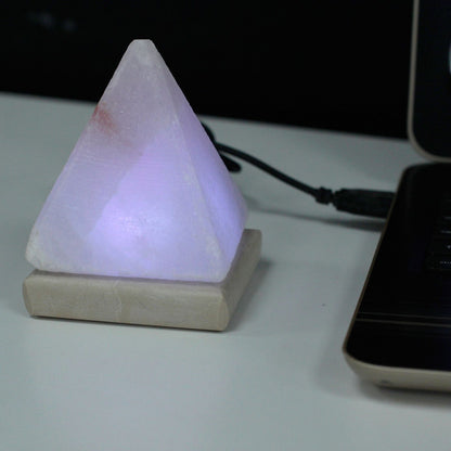 White pyramid Himalayan salt lamp cycling through rainbow colours, pink salt crystal glowing inside, USB cable, on minimalist white desk with laptop