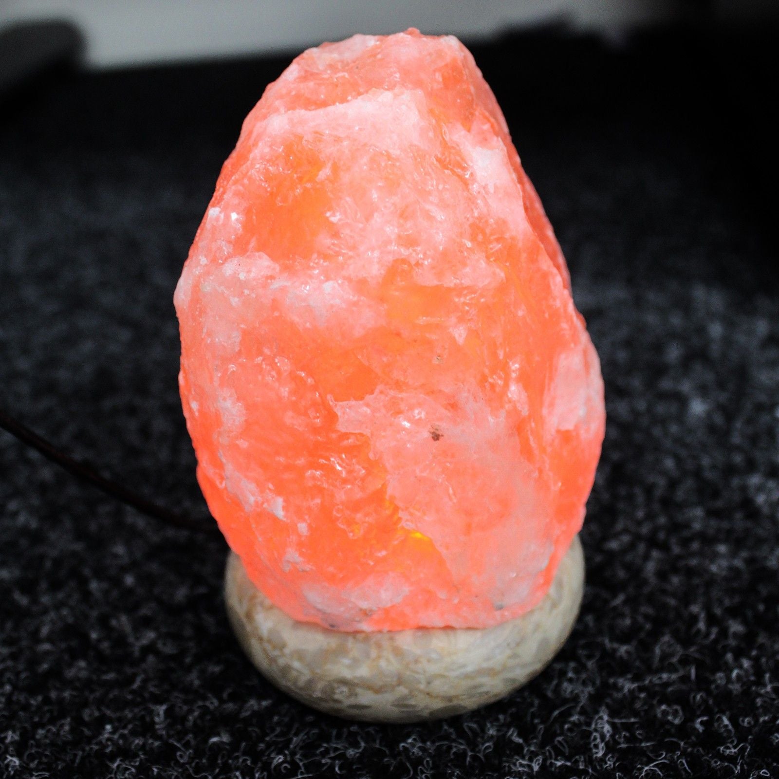 Natural-shaped pink Himalayan salt lamp glowing softly on wooden base with USB cable