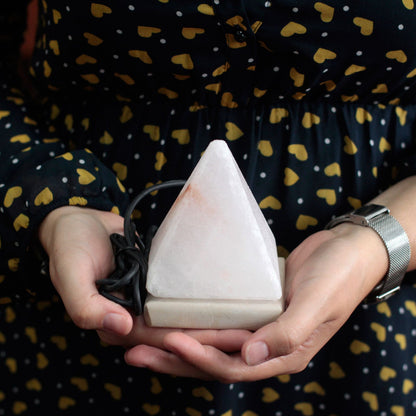 Person holding a triangular white pyramid Himalayan salt lamp cycling through rainbow colours, pink salt crystal glowing inside, USB cable