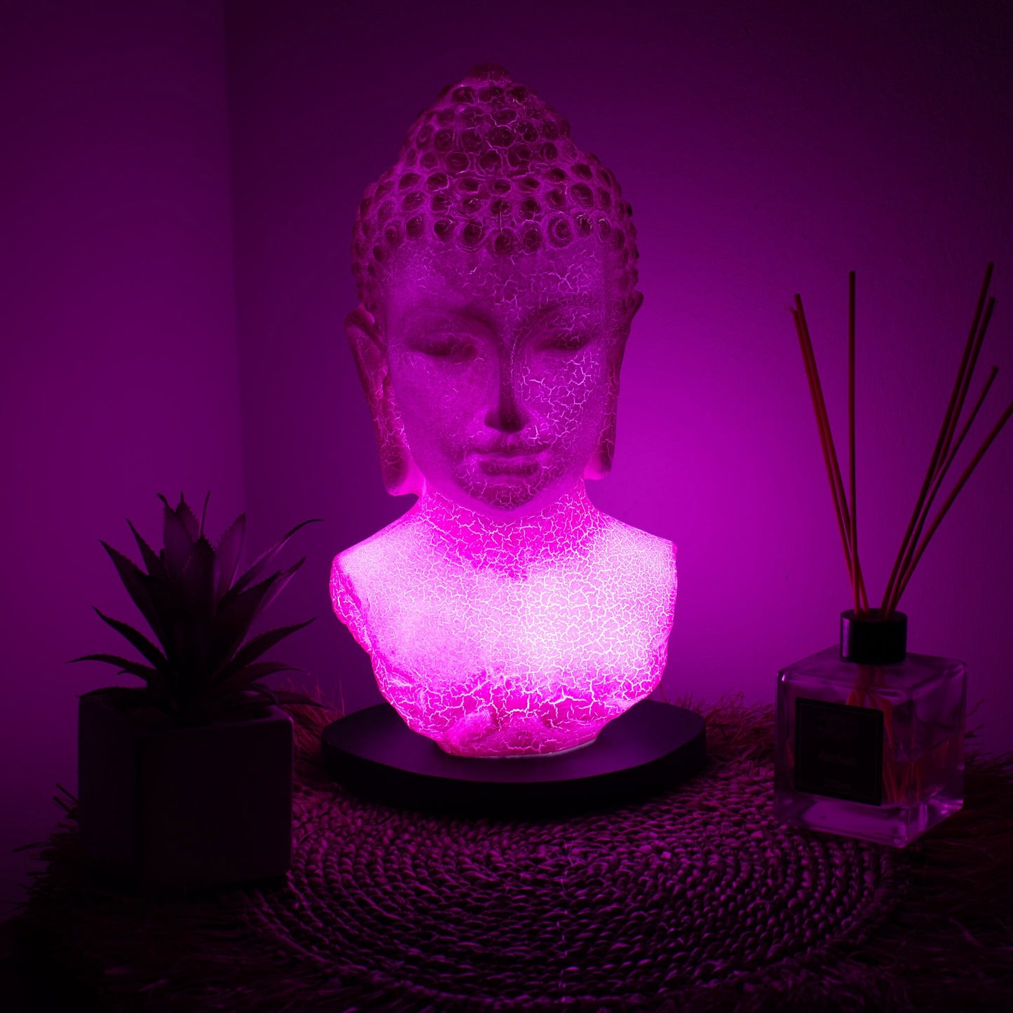 Buddha Bust Lamp with crackle textured surface on modern oval stand, emitting soft warm ambient glow in a calm living space with subtle lighting
