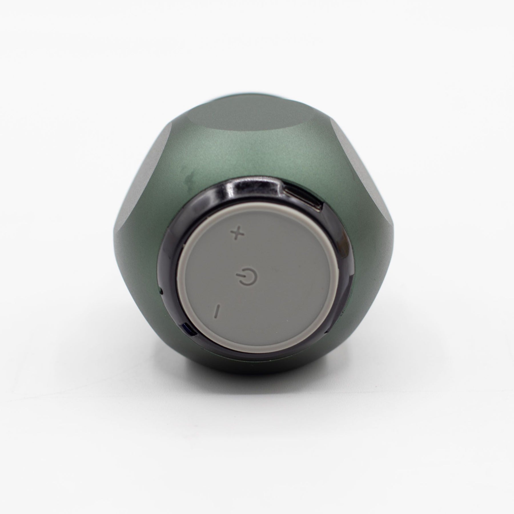 Close-up of green mini speaker showing carry hook, speaker grille, top controls (play/pause/volume) and Bluetooth pairing LED