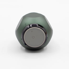 Close-up of green mini speaker showing carry hook, speaker grille, top controls (play/pause/volume) and Bluetooth pairing LED