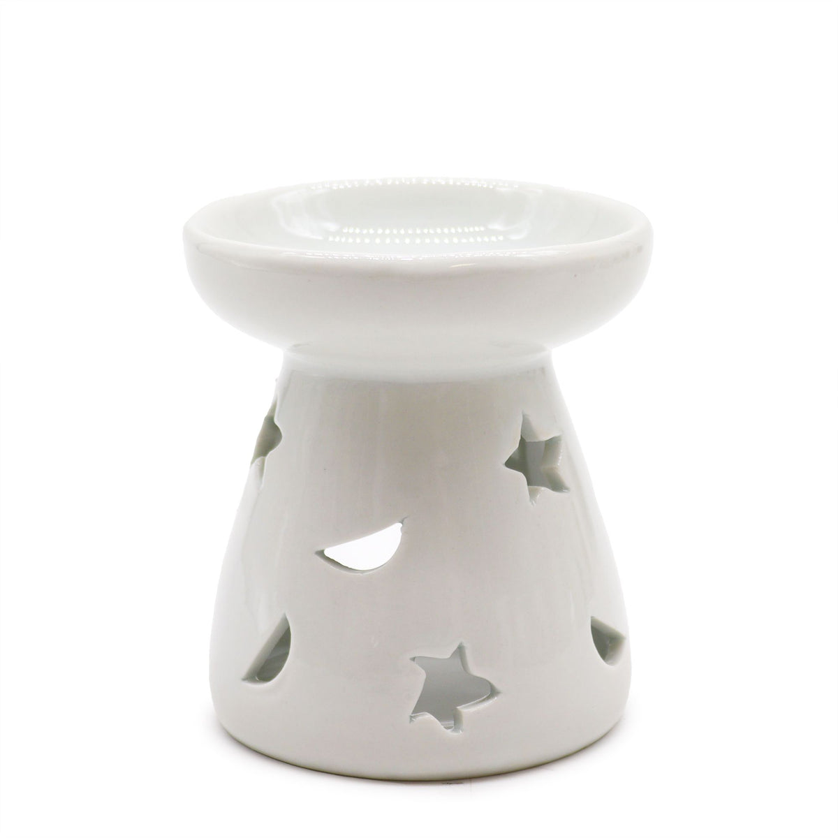 Classic white ceramic oil burner with moon and star cut-out design glowing with tealight on cosy winter evening table