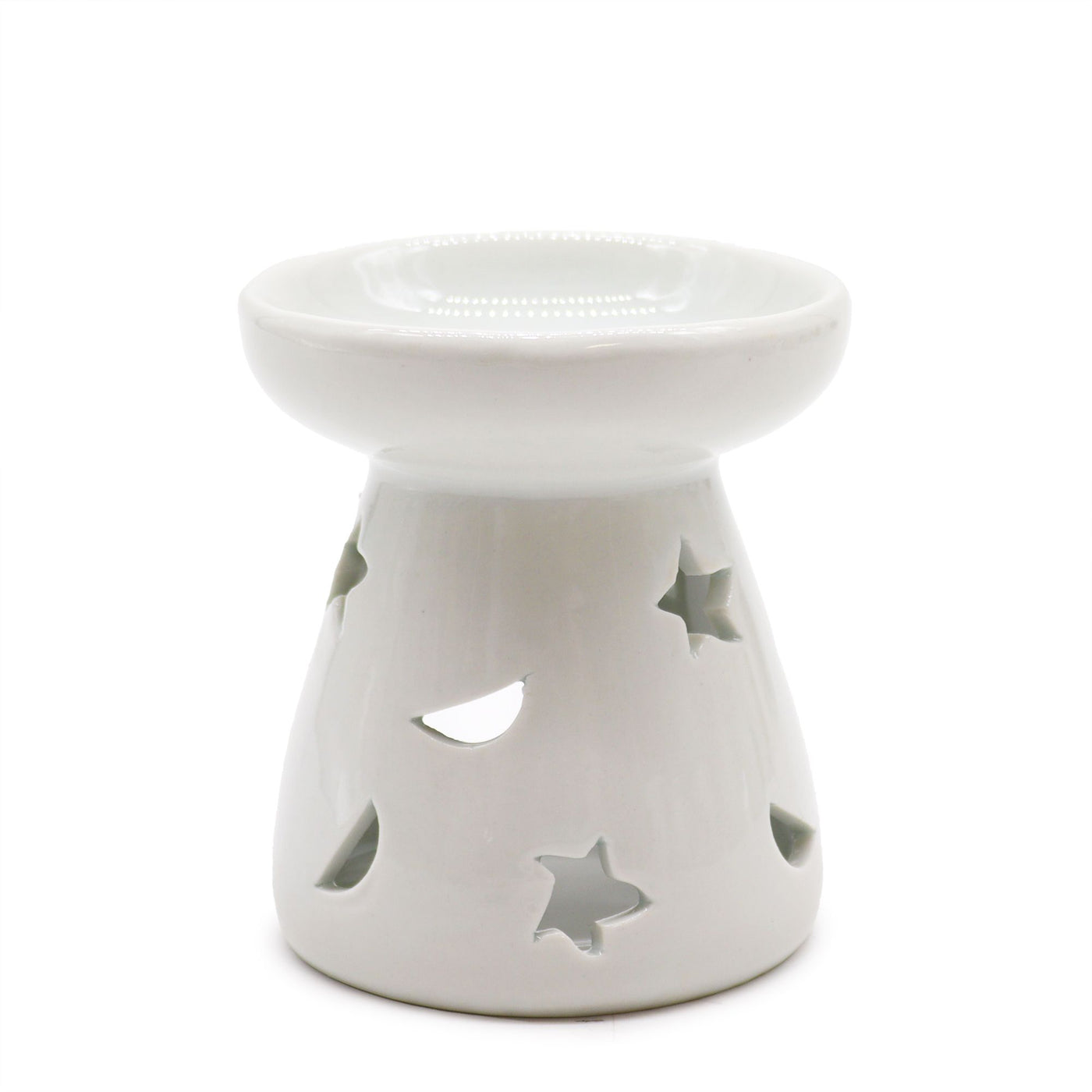 Classic white ceramic oil burner with moon and star cut-out design glowing with tealight on cosy winter evening table