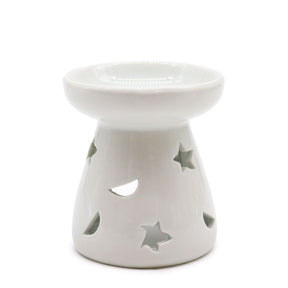 Classic white ceramic oil burner with moon and star cut-out design glowing with tealight on cosy winter evening table