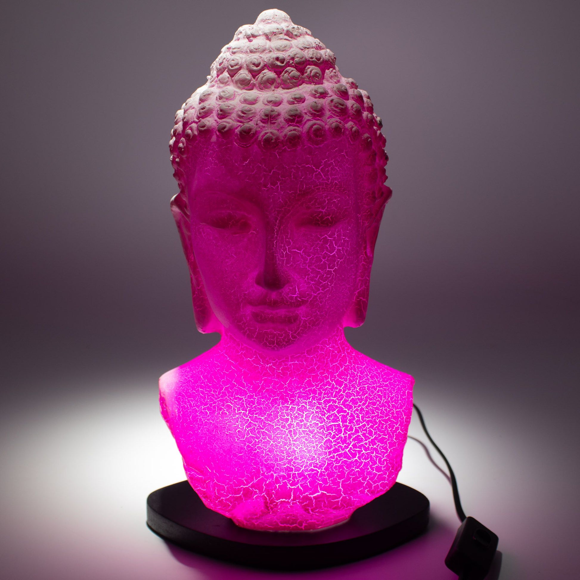 Buddha Bust Lamp with crackle textured surface on modern oval stand, emitting soft warm ambient glow in a calm living space with subtle lighting