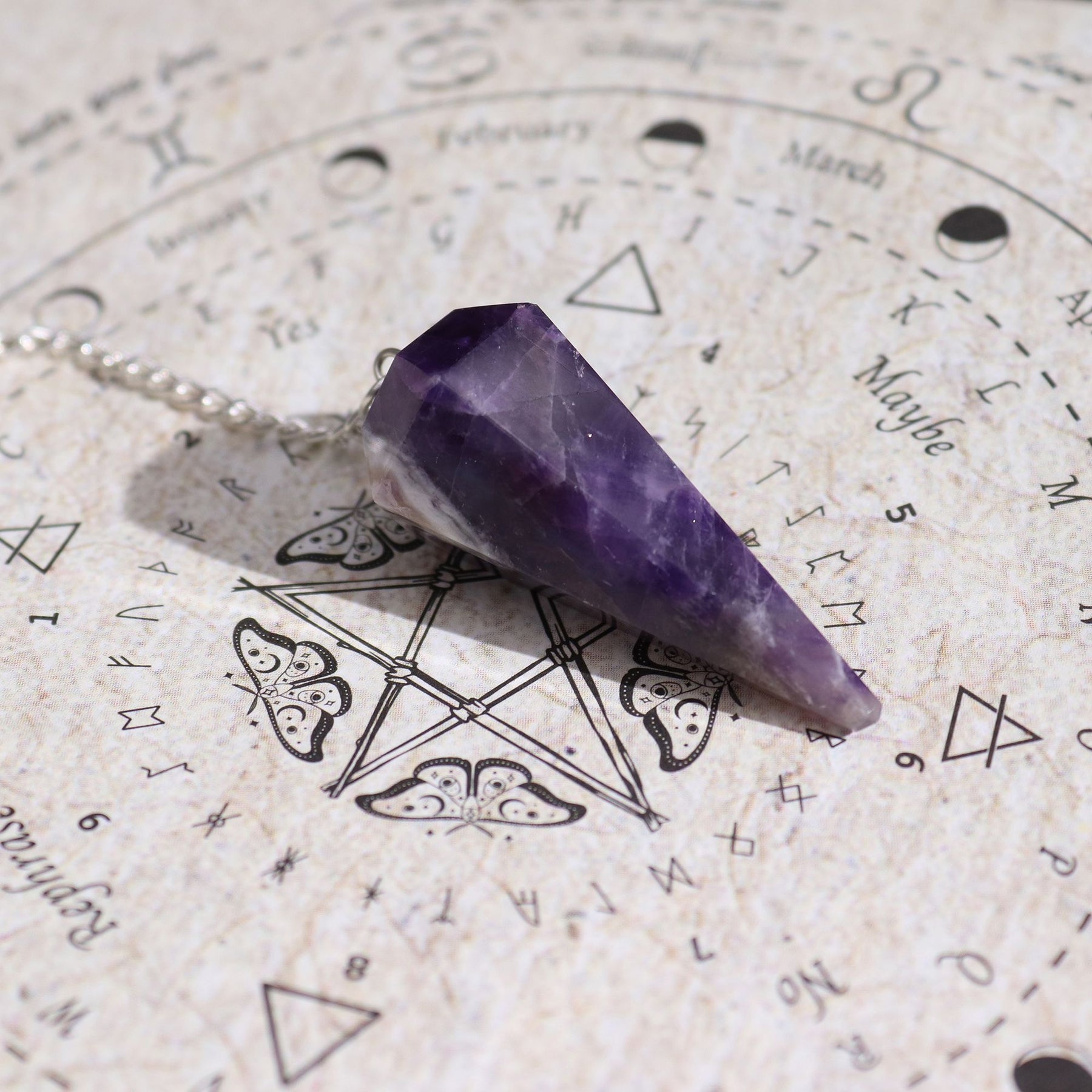 Amethyst crystal pendulum on an astrological chart