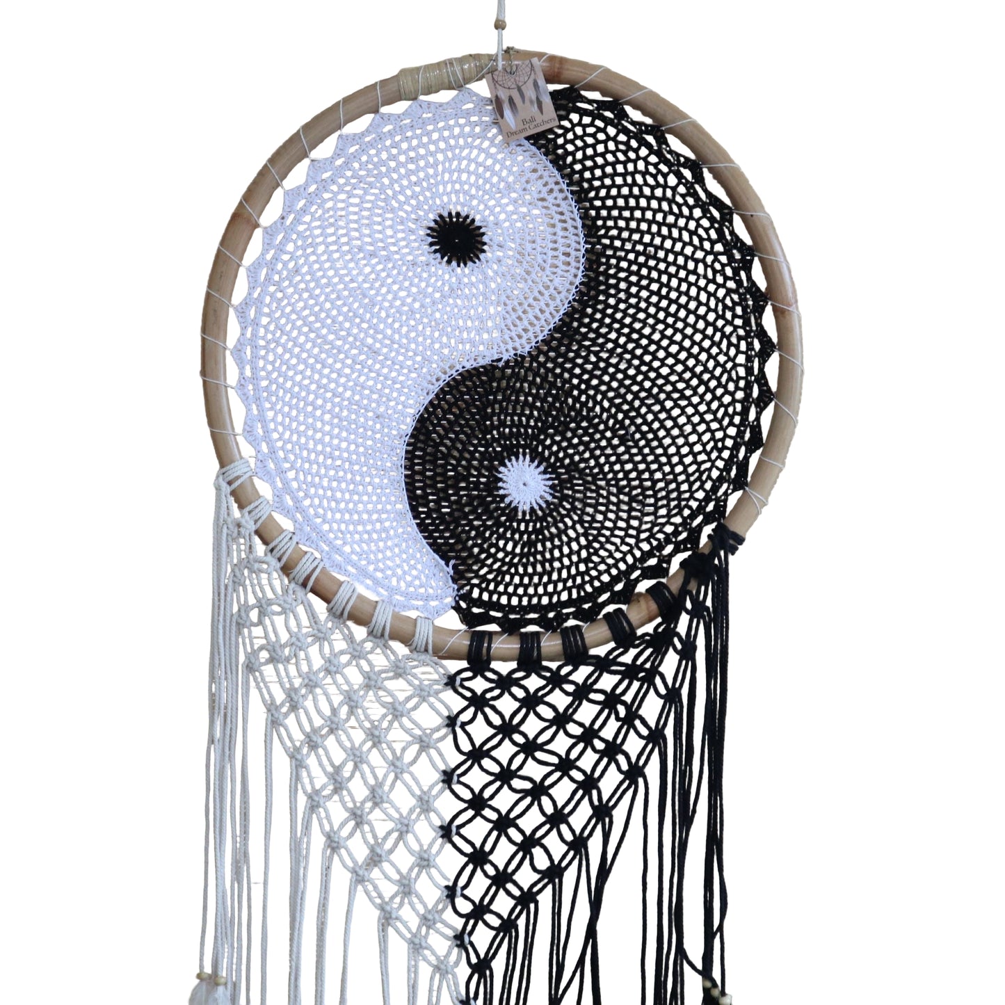 Extra large black and white Yin Yang dream catcher hanging above bed with flowing feathers and wooden beads against white wall