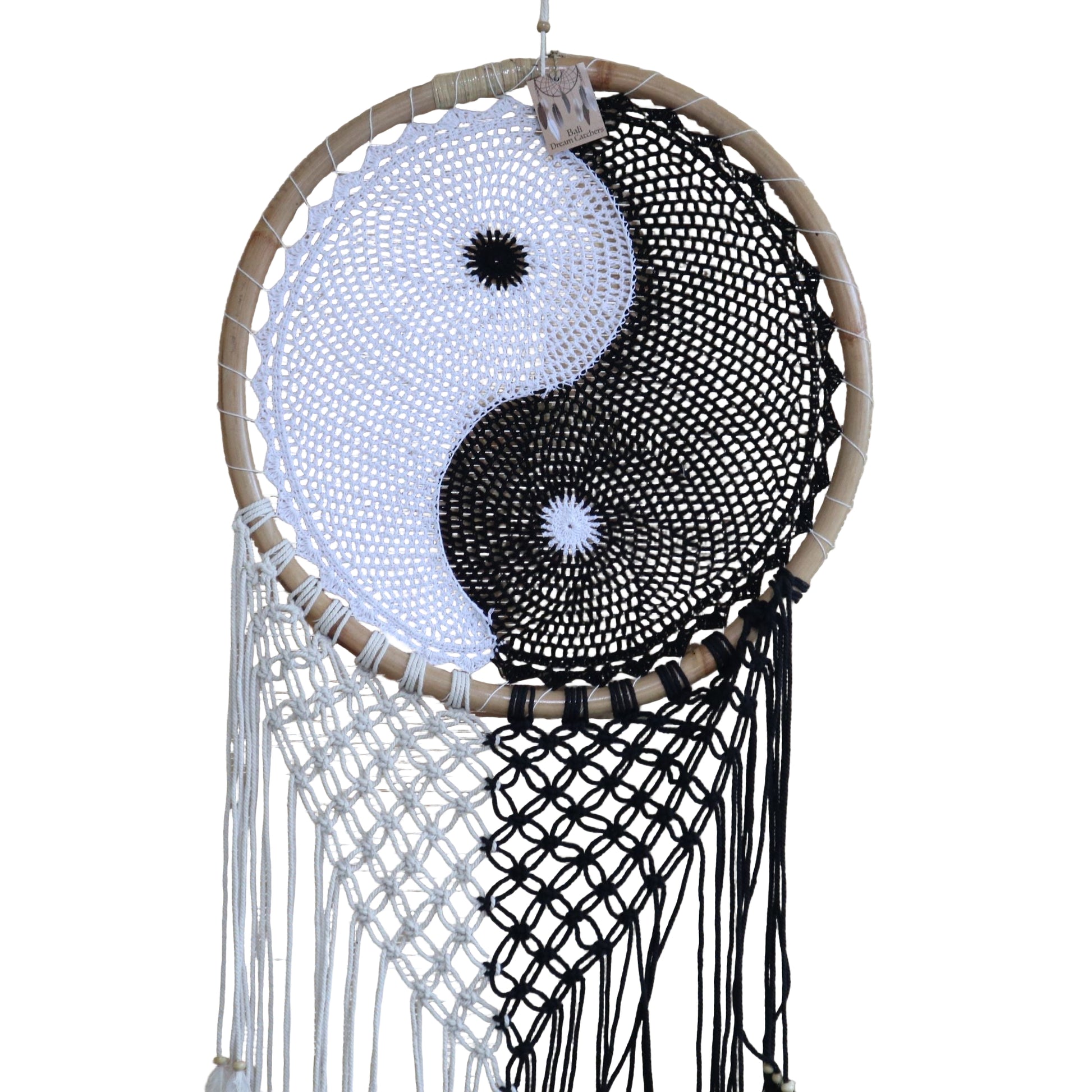 Extra large black and white Yin Yang dream catcher hanging above bed with flowing feathers and wooden beads against white wall