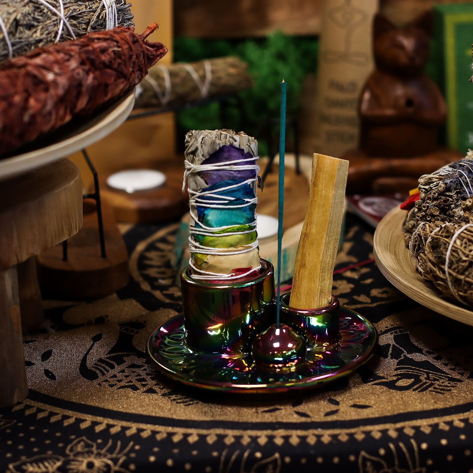 Metallic rainbow mandala ceramic smudge holder with iridescent colour-shift finish, Palo Santo stick burning, sage bundle and incense cone, styled on altar with crystals and candles
