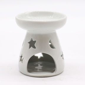 Classic white ceramic oil burner with moon and star cut-out design glowing with tealight on cosy winter evening table