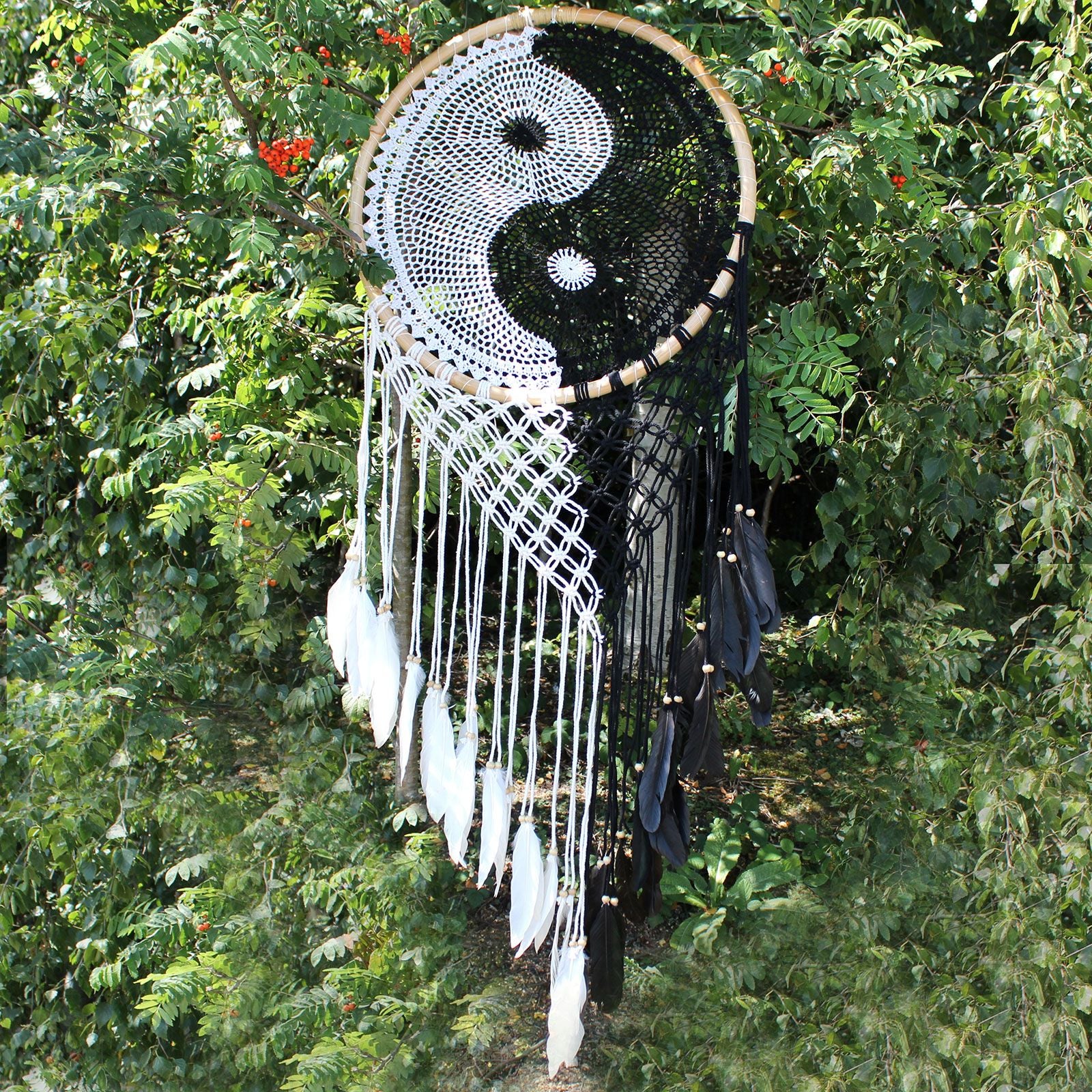 Extra large black and white Yin Yang dream catcher hanging above bed with flowing feathers and wooden beads against white wall