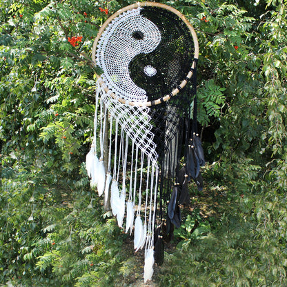 Extra large black and white Yin Yang dream catcher hanging above bed with flowing feathers and wooden beads against white wall