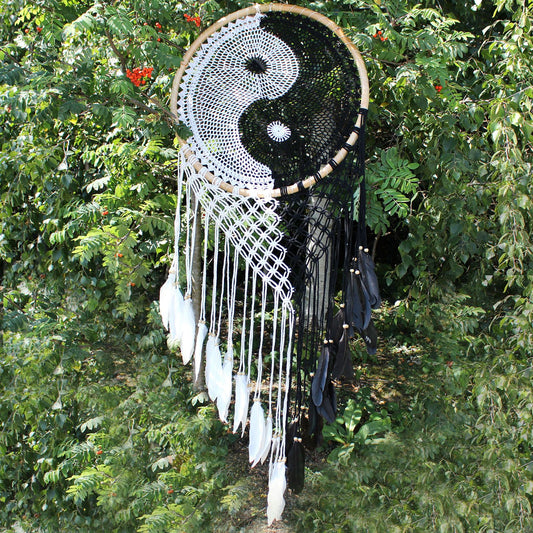 Extra large black and white Yin Yang dream catcher hanging above bed with flowing feathers and wooden beads against white wall
