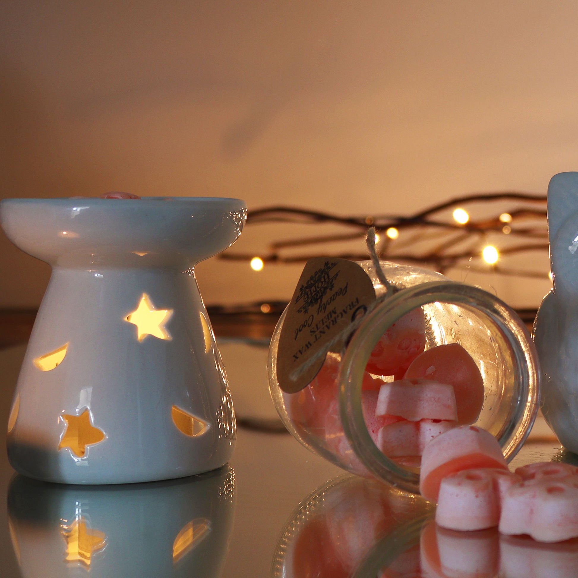 Classic white ceramic oil burner with moon and star cut-out design glowing with tealight on cosy winter evening table