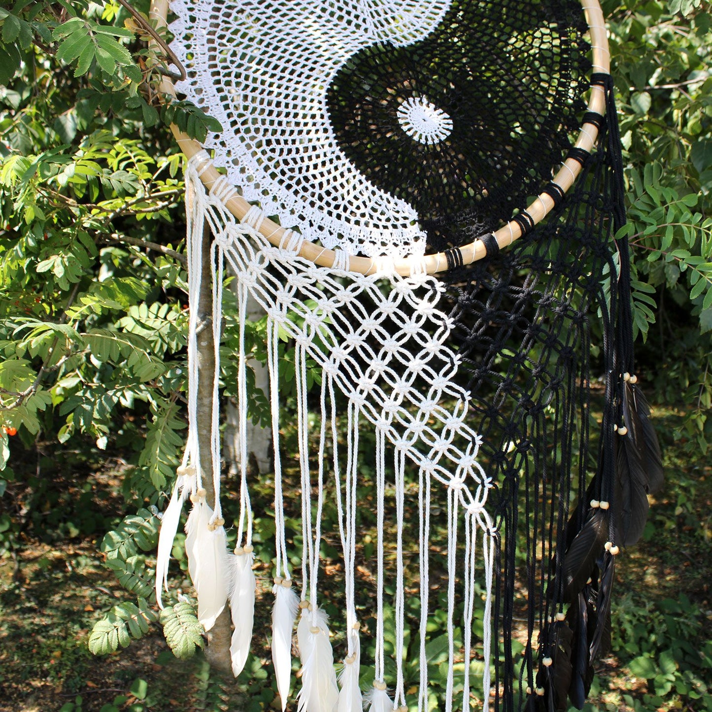 Extra large black and white Yin Yang dream catcher hanging above bed with flowing feathers and wooden beads against white wall