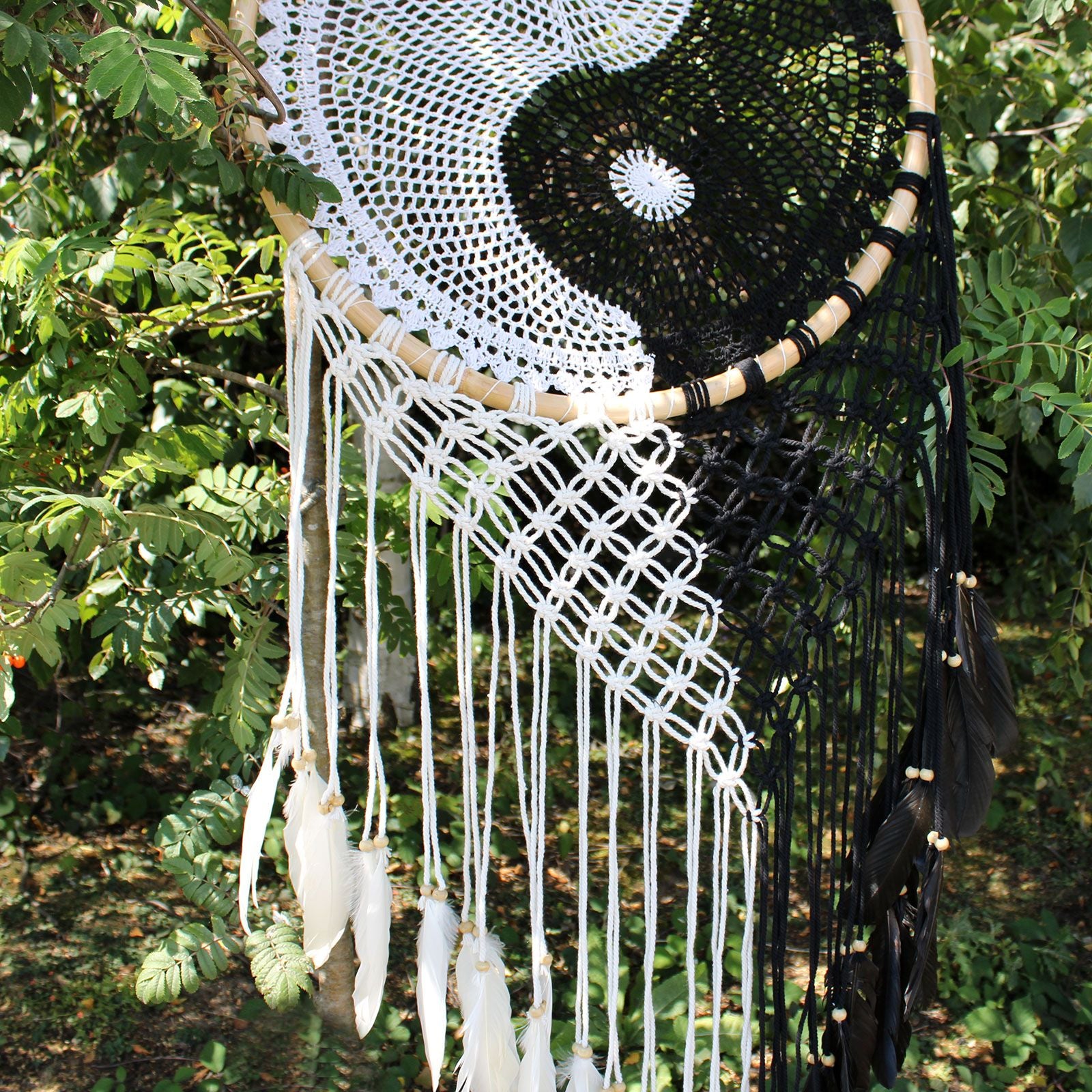 Extra large black and white Yin Yang dream catcher hanging above bed with flowing feathers and wooden beads against white wall