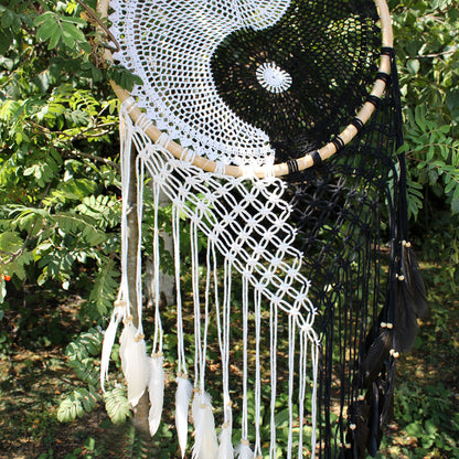 Extra large black and white Yin Yang dream catcher hanging above bed with flowing feathers and wooden beads against white wall