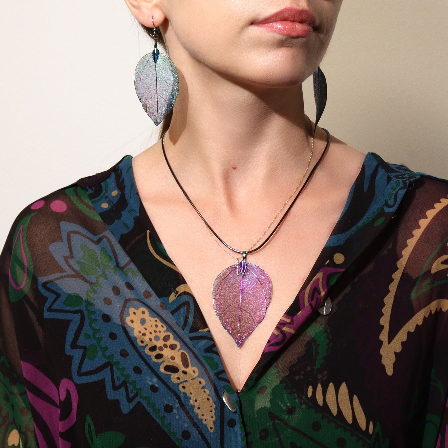 Person wearing a colorful patterned garment with a leaf-shaped necklace and earrings.