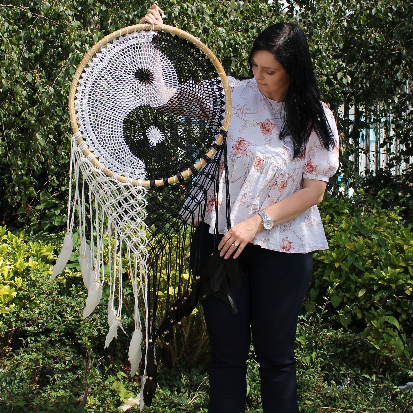 Extra large black and white Yin Yang dream catcher hanging above bed with flowing feathers and wooden beads against white wall